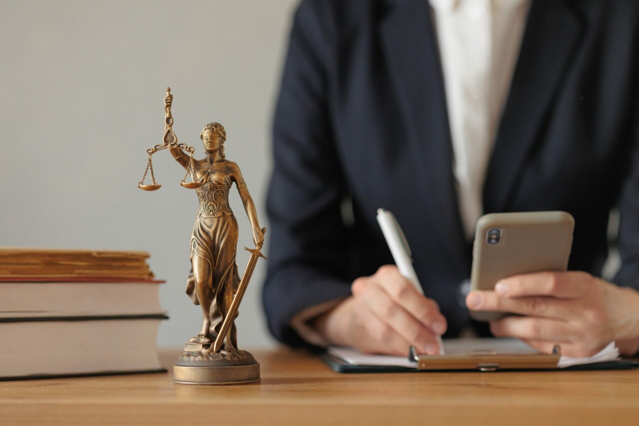 lawyer works on phone next to small statue of lady justice