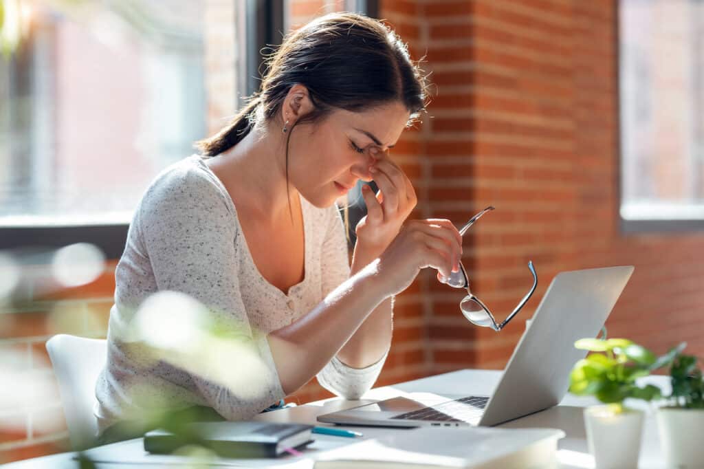 Tired employee sitting at her desk with a headache from technology